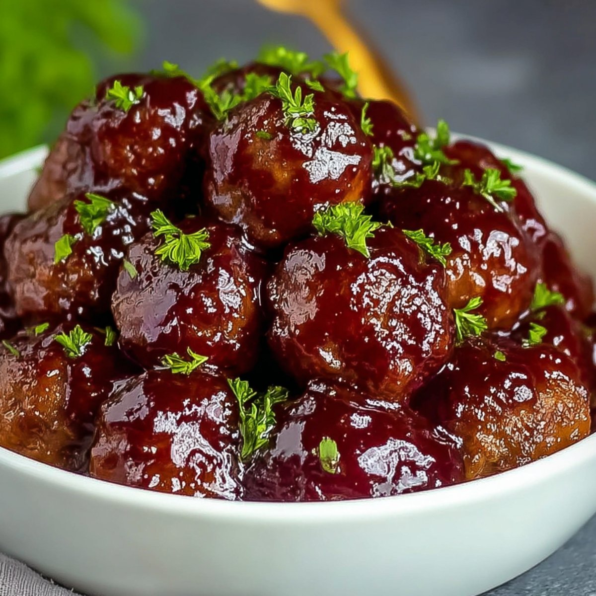 Bowl of glossy grape jelly meatballs garnished with fresh parsley, ready to serve.