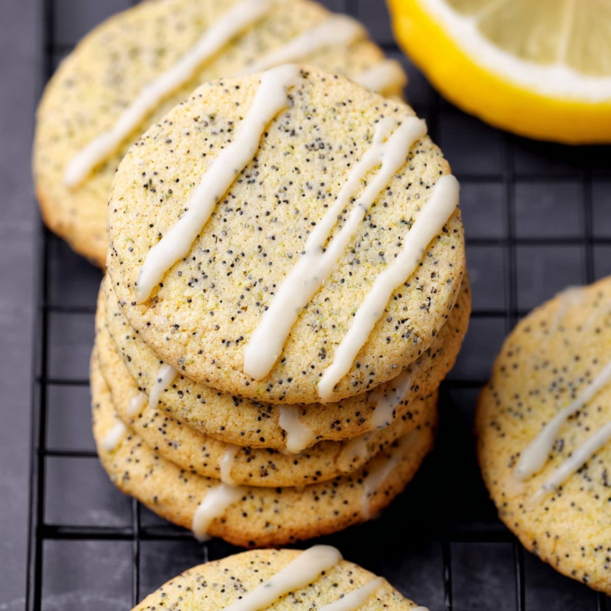 Round cookies speckled with Poppy seeds and topped with Lemon Poppy Seed Cookies glaze, stacked on a black wire cooling rack.
