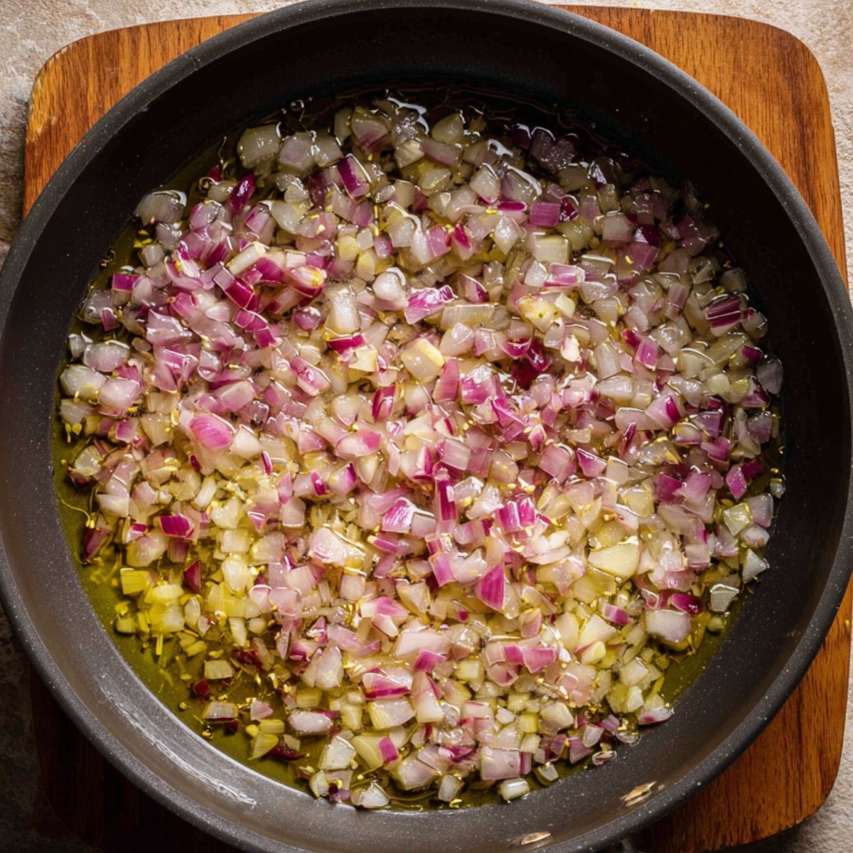 Close-up of diced onions cooking in olive oil in a pan, starting to soften and turn translucent.
