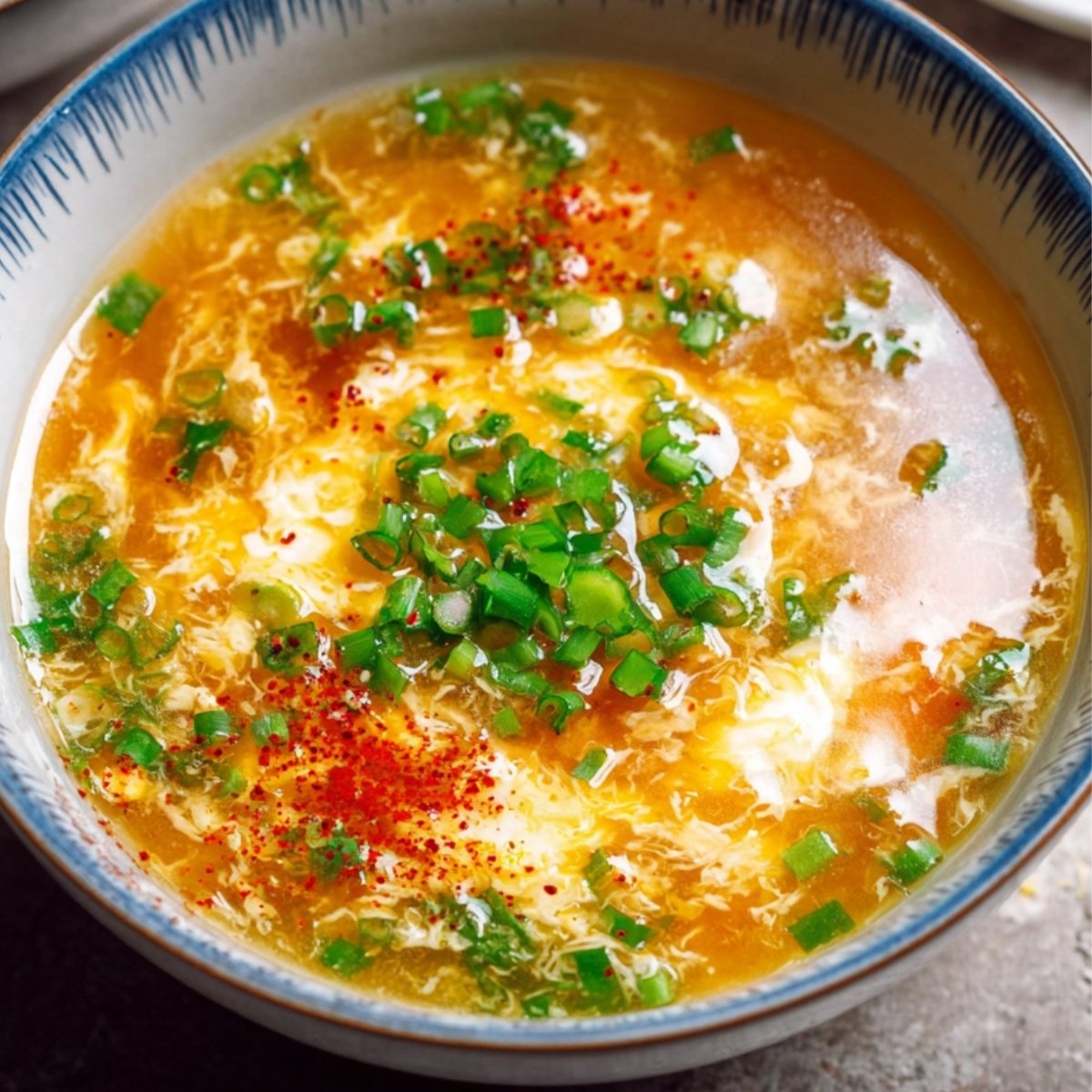 Egg drop soup a serving bowl of egg drop soup garnished with chopped green onions and red chili flakes for spice.