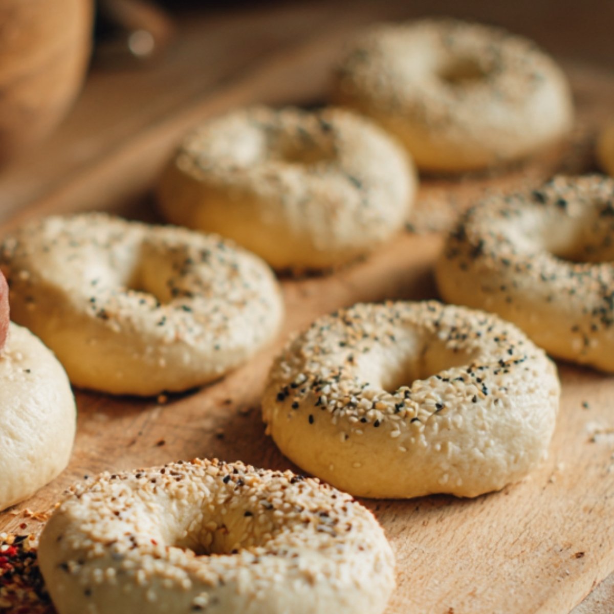 "Unbaked bagels sprinkled with sesame and poppy seeds on a wooden board, ready for baking."