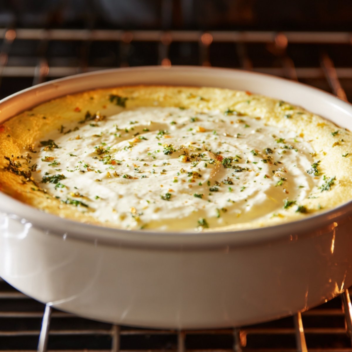 A fluffy eggs benedict casserole baking in the oven, garnished with herbs and a creamy sauce layer on top.