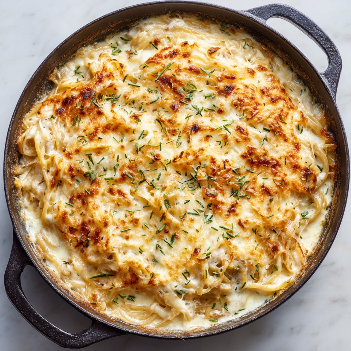 A bubbling skillet of creamy French onion pasta topped with melted golden cheese and sprinkled with fresh herbs.