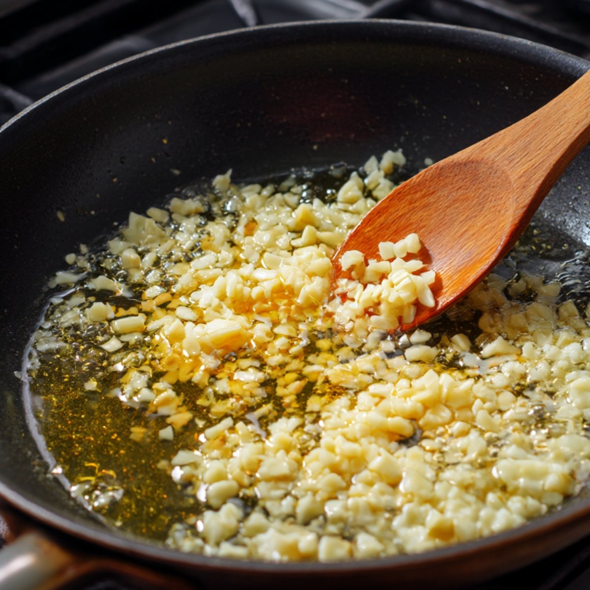 Chopped garlic sizzling in oil in a frying pan. The garlic pieces are golden and aromatic, frying to release their flavor in preparation for a spicy dish like Tteokbokki. The kitchen stove is visible in the background.