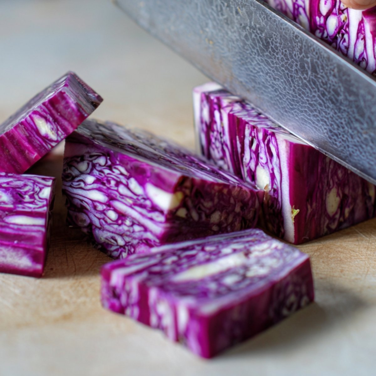 Close-up of a knife slicing through fresh purple cabbage, revealing intricate patterns inside the cut pieces.