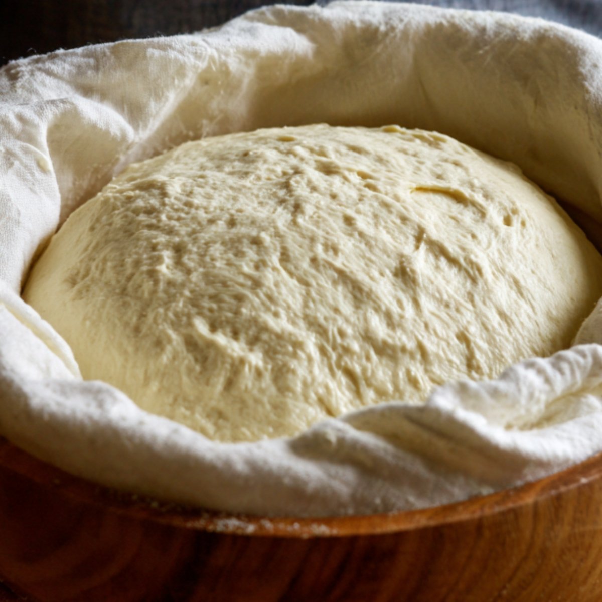 "Fluffy bread dough doubled in size during first rise inside a cloth-lined bowl."