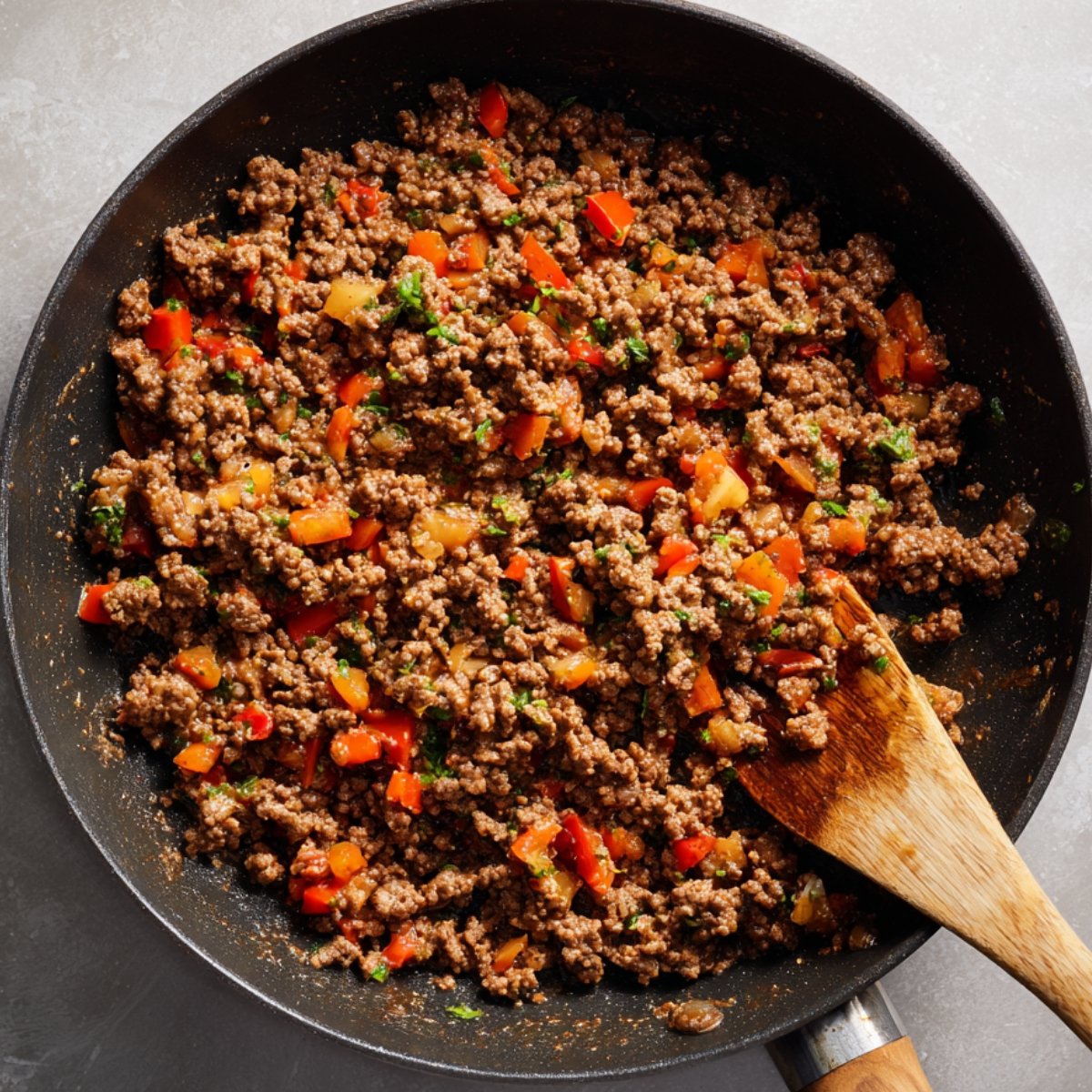 Skillet of ground beef mixed with diced peppers and taco seasoning.