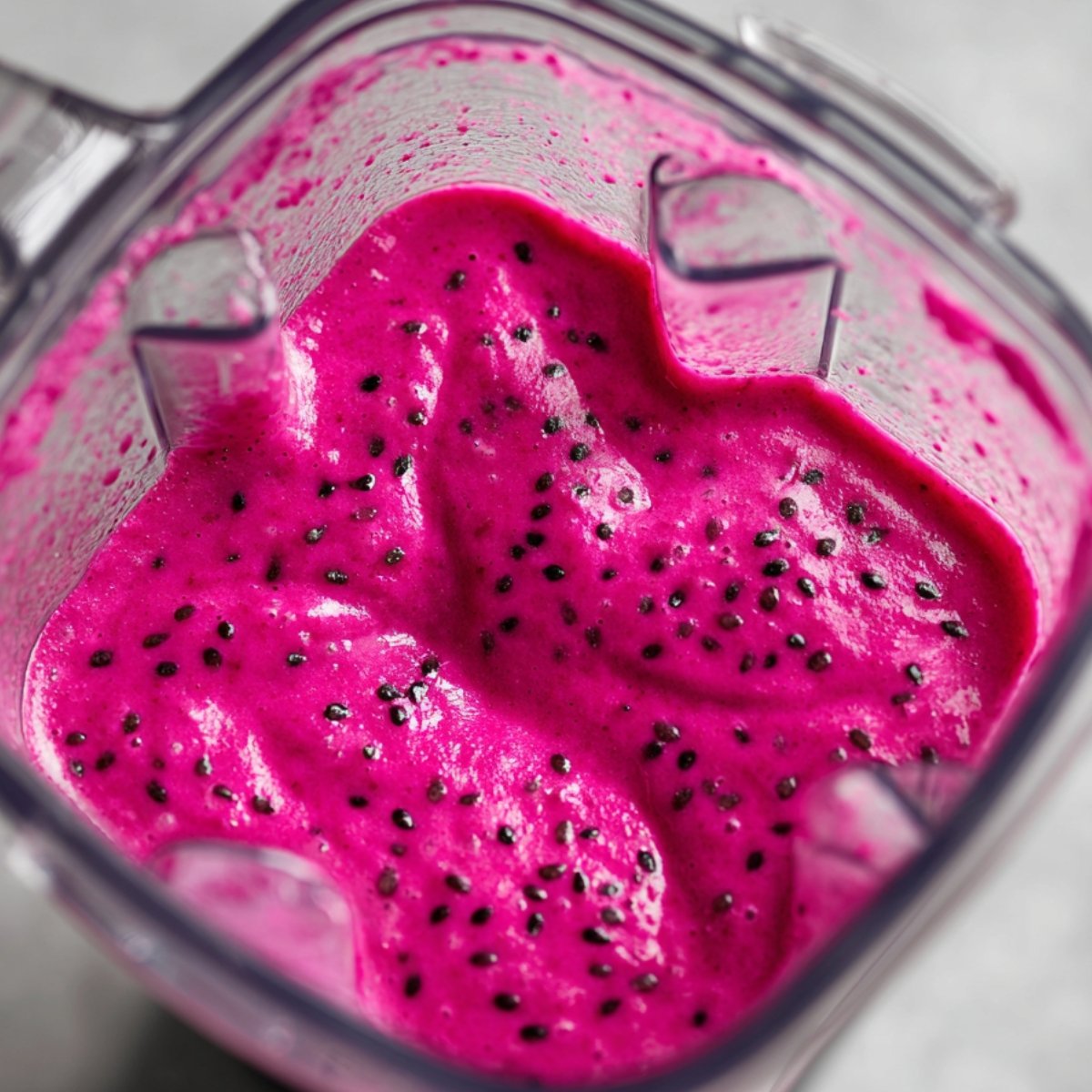"Blender container with thick, creamy dragon fruit smoothie showing a vibrant pink color with black seeds."