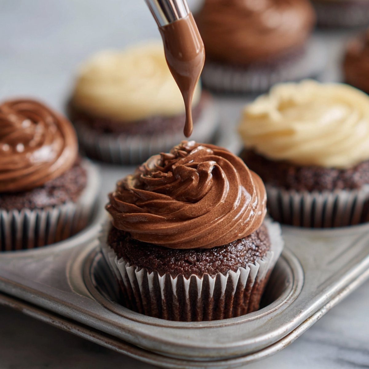 Chocolate cupcakes being frosted with a piping bag, showing swirls of chocolate and vanilla frosting.