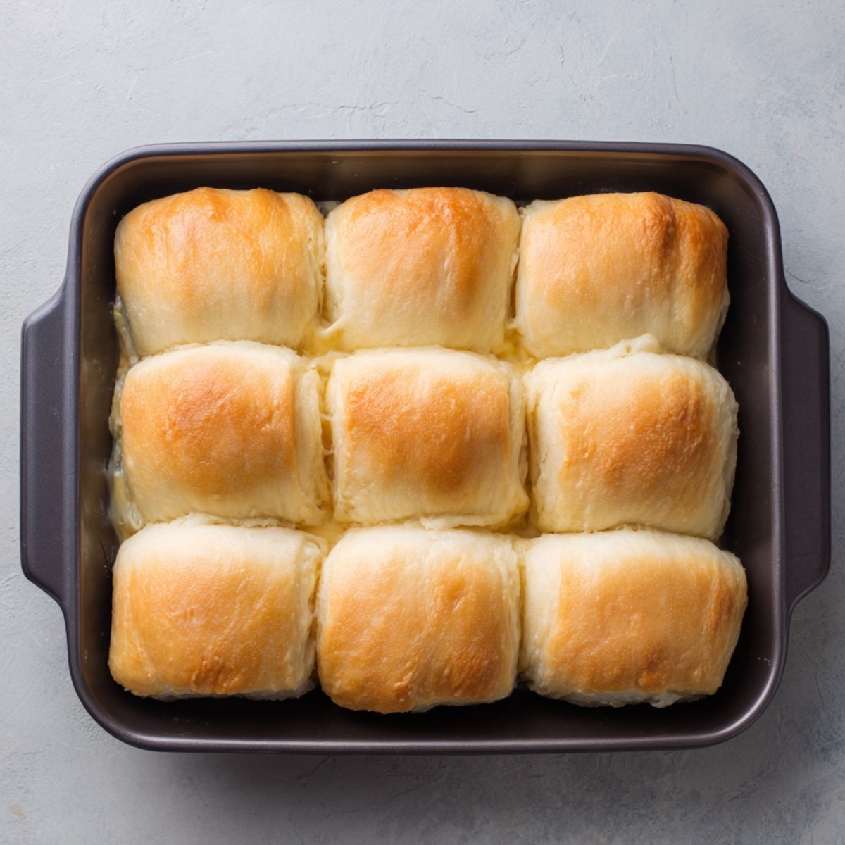 A tray of freshly baked, fluffy golden crescent rolls in a rectangular baking dish.