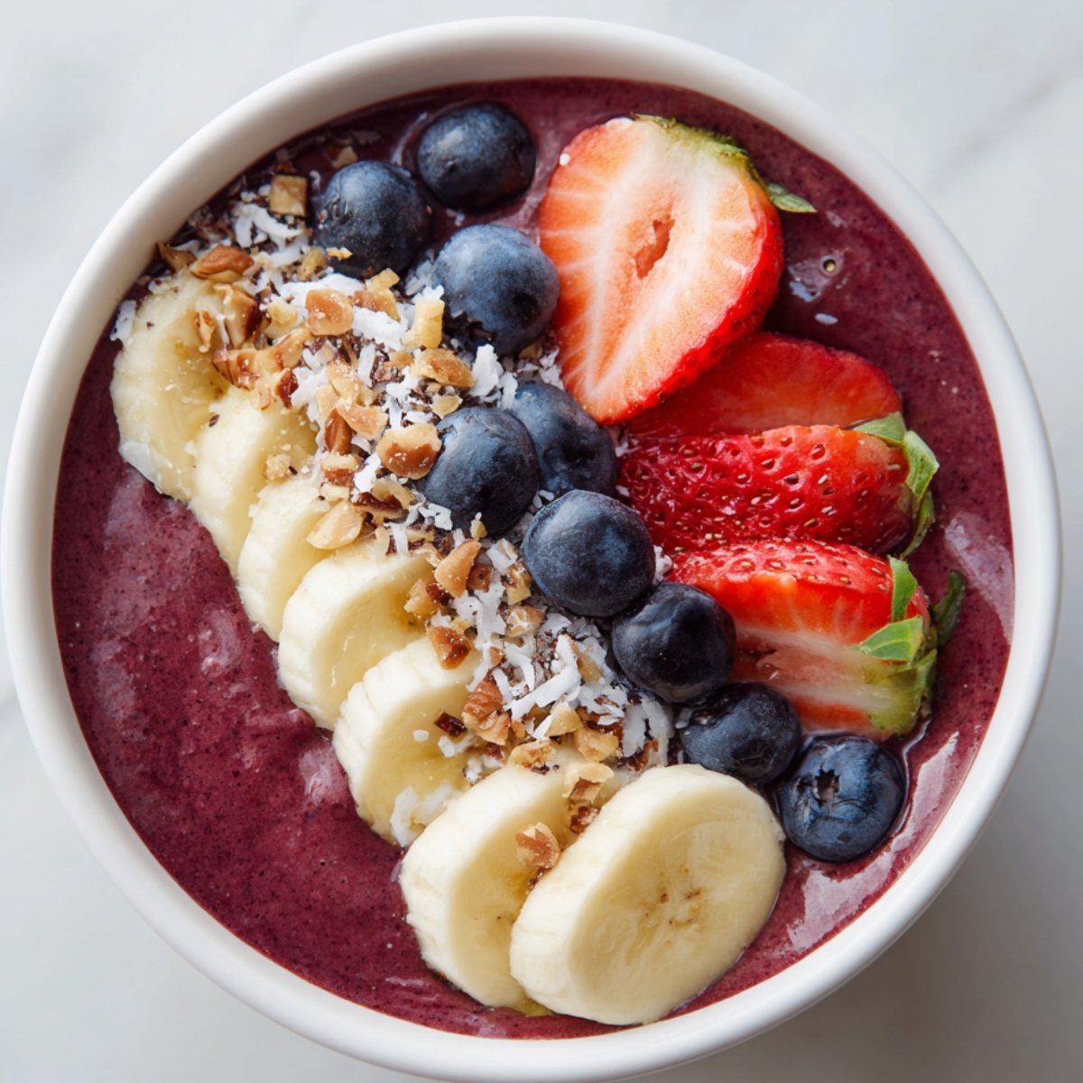 A classic acai bowl topped with banana slices, strawberries, blueberries, shredded coconut, and granola.