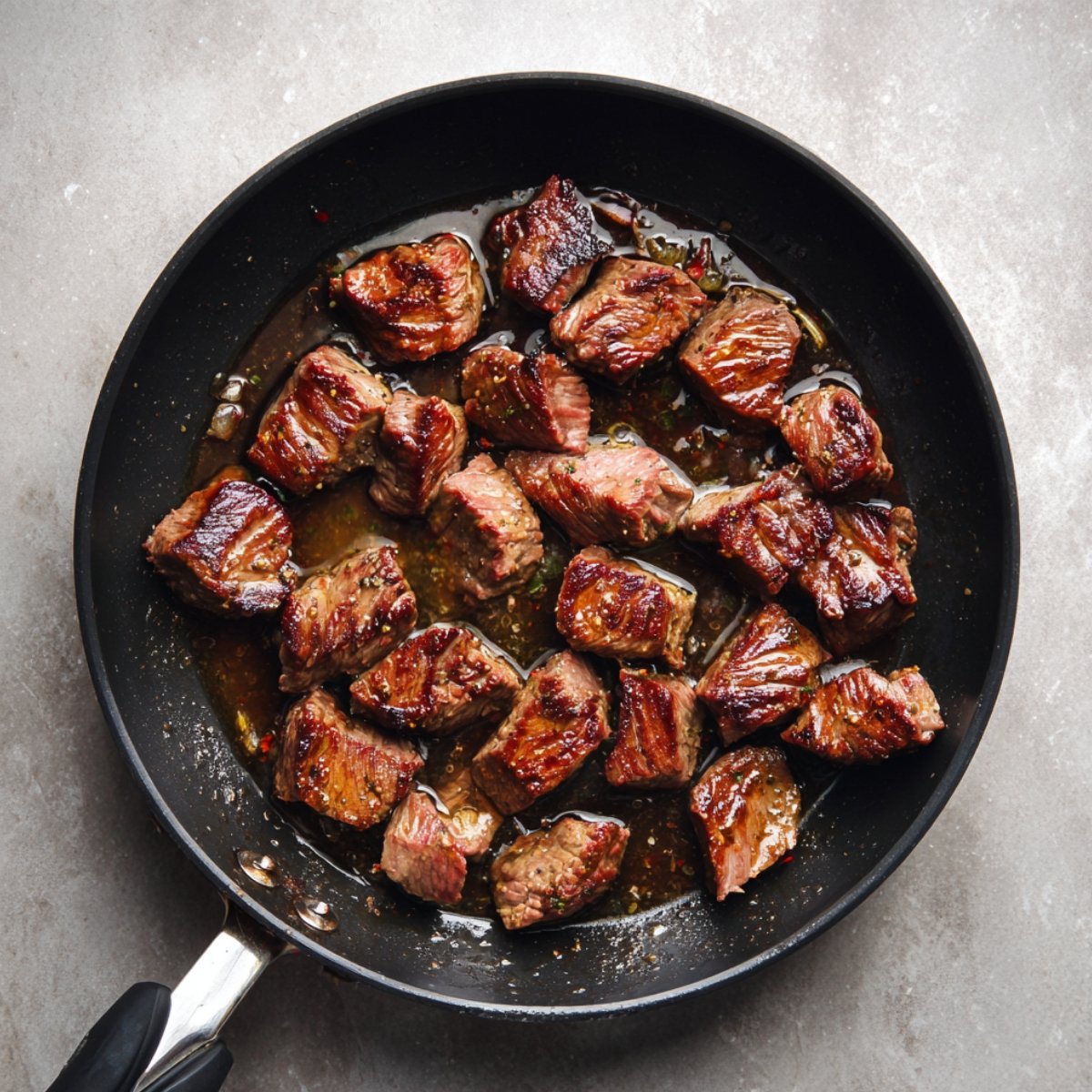 “Golden brown seared beef cubes sizzling in a black skillet with juices.”