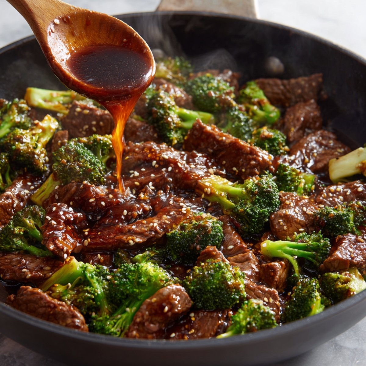 “Wooden spoon pouring savory brown sauce over beef and broccoli stir fry in skillet.”