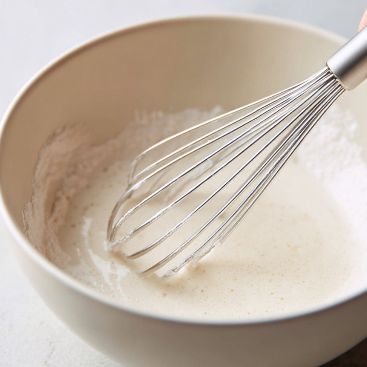 A whisk mixing cornstarch and water in a small bowl to make the thickener for egg drop soup.