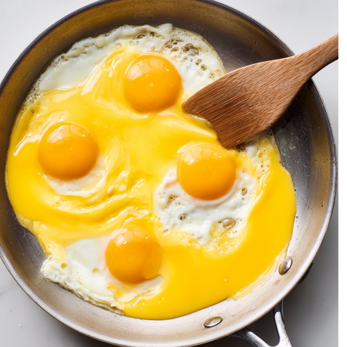 Raw eggs being stirred in a frying pan with a wooden spatula.