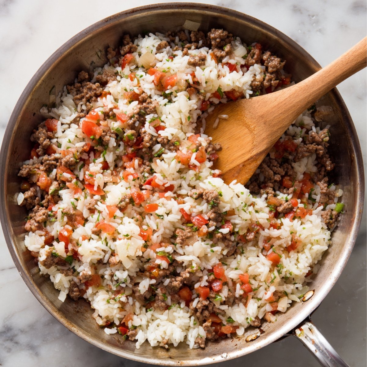 “Ground beef, rice, tomatoes, and herbs cooking together in skillet for stuffed pepper filling.”
