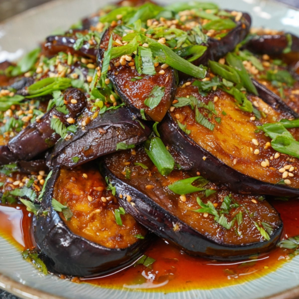 A plate of braised Japanese eggplant recipe in a red soy-based sauce, topped with sesame seeds, scallions, and herbs.