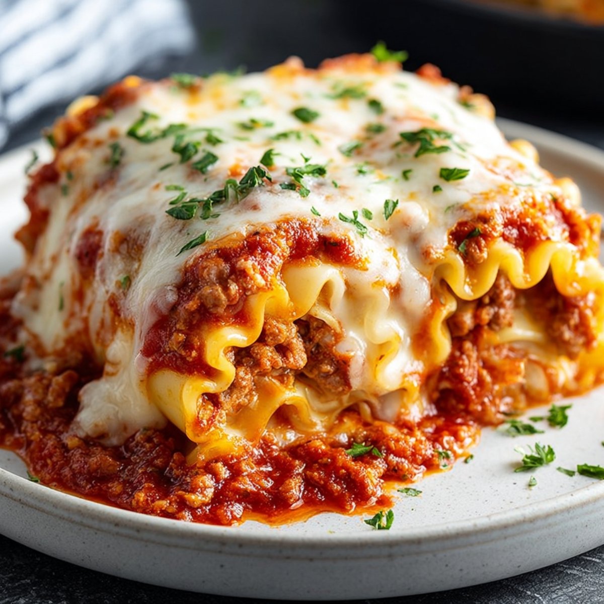 "Close-up of cheesy, baked lasagna roll ups with meat sauce and herbs, served on a white plate."