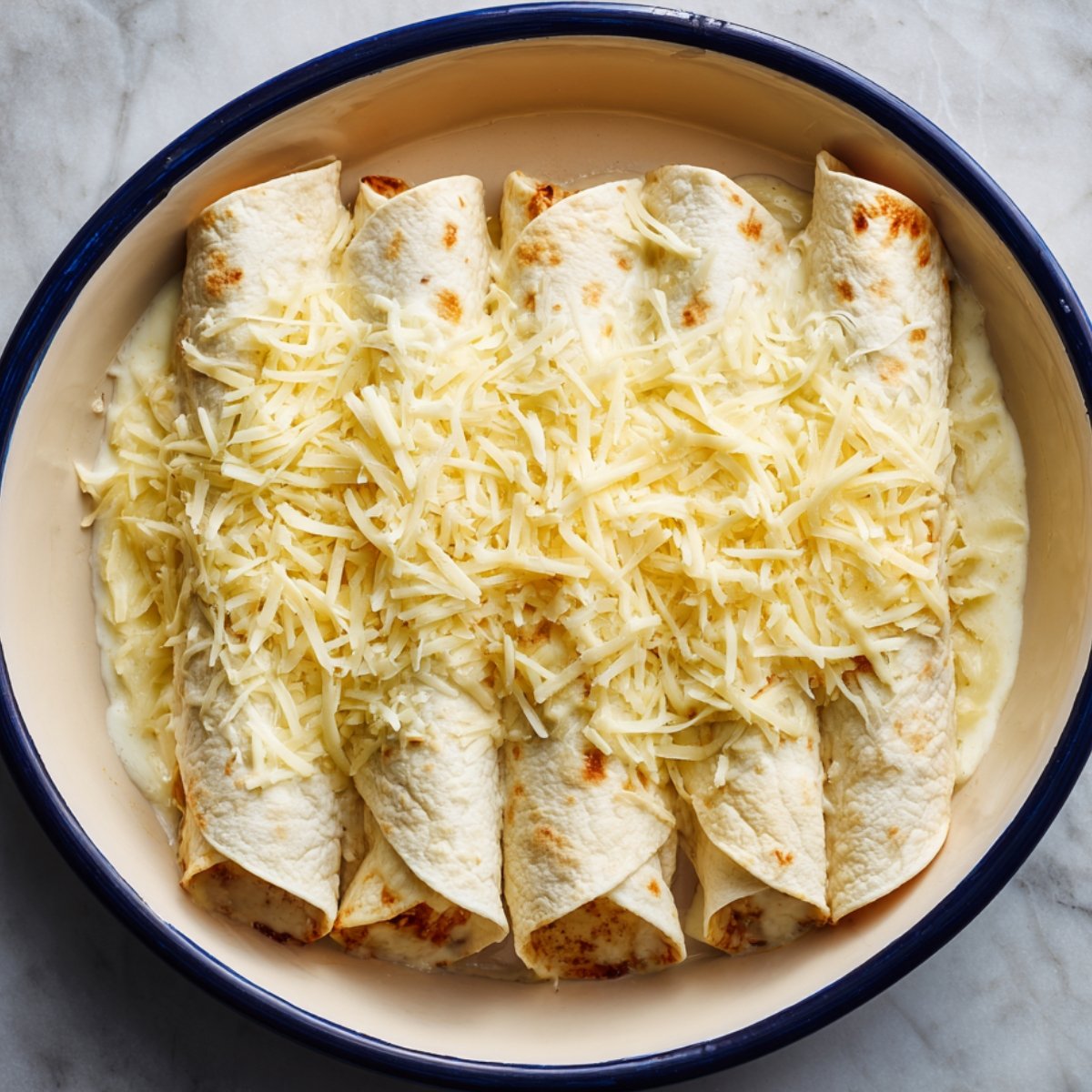 A skillet filled with cooked chicken pieces mixed with shredded cheese and herbs, being prepared for enchilada filling.