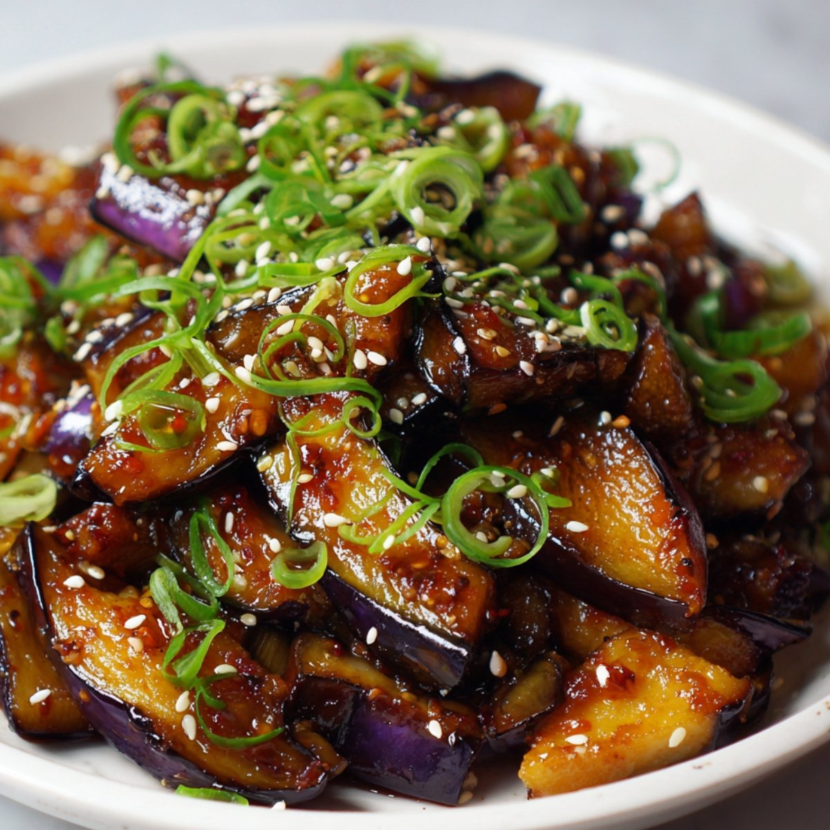 A plate of glazed stir-fried Japanese eggplant garnished with sesame seeds and thinly sliced green onions.