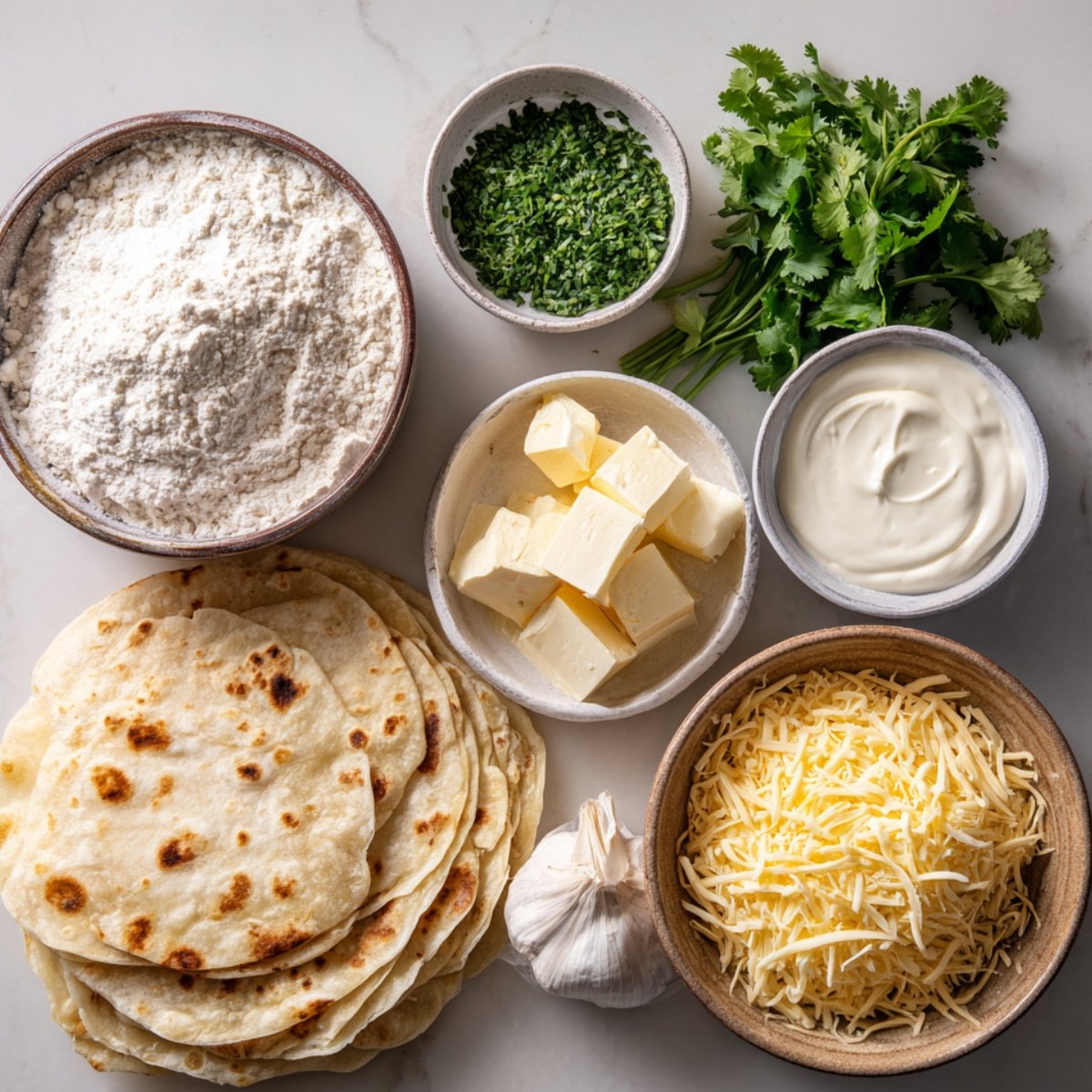 Ingredients for creamy white chicken enchiladas including flour tortillas, shredded cheese, butter, sour cream, garlic, flour, and fresh cilantro arranged on a table.
