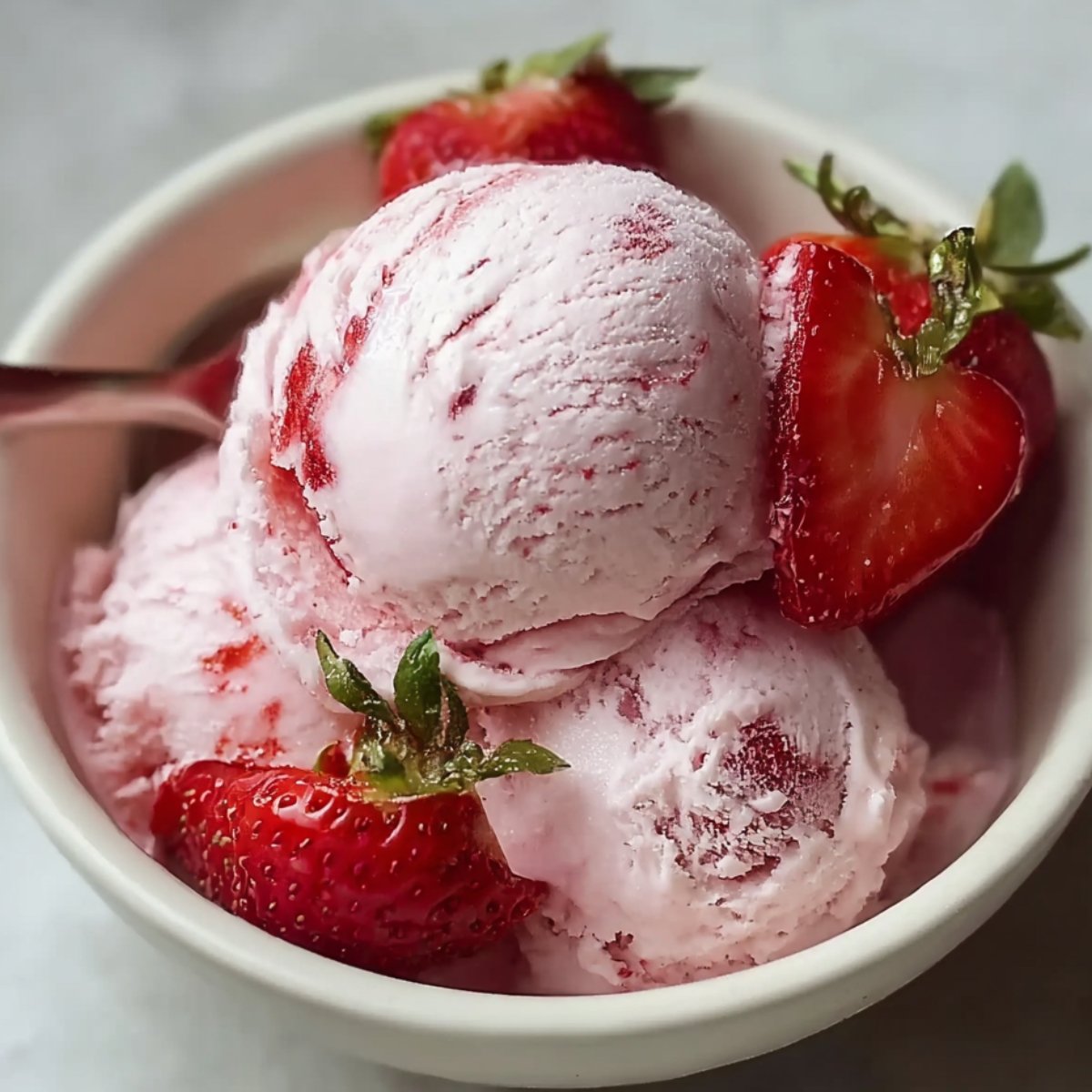 A bowl of homemade strawberry ice cream with a scoop of pink ice cream, garnished with fresh strawberries.