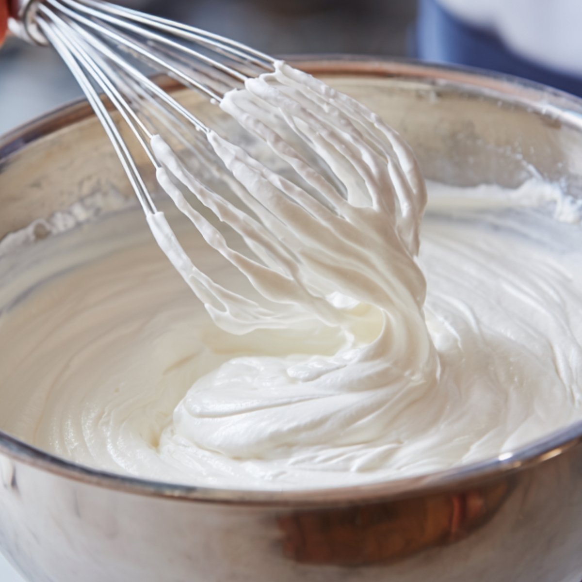 A whisk gently mixing a bowl of whipped cream, creating a smooth, fluffy texture, showing the creamy consistency of the mixture.
