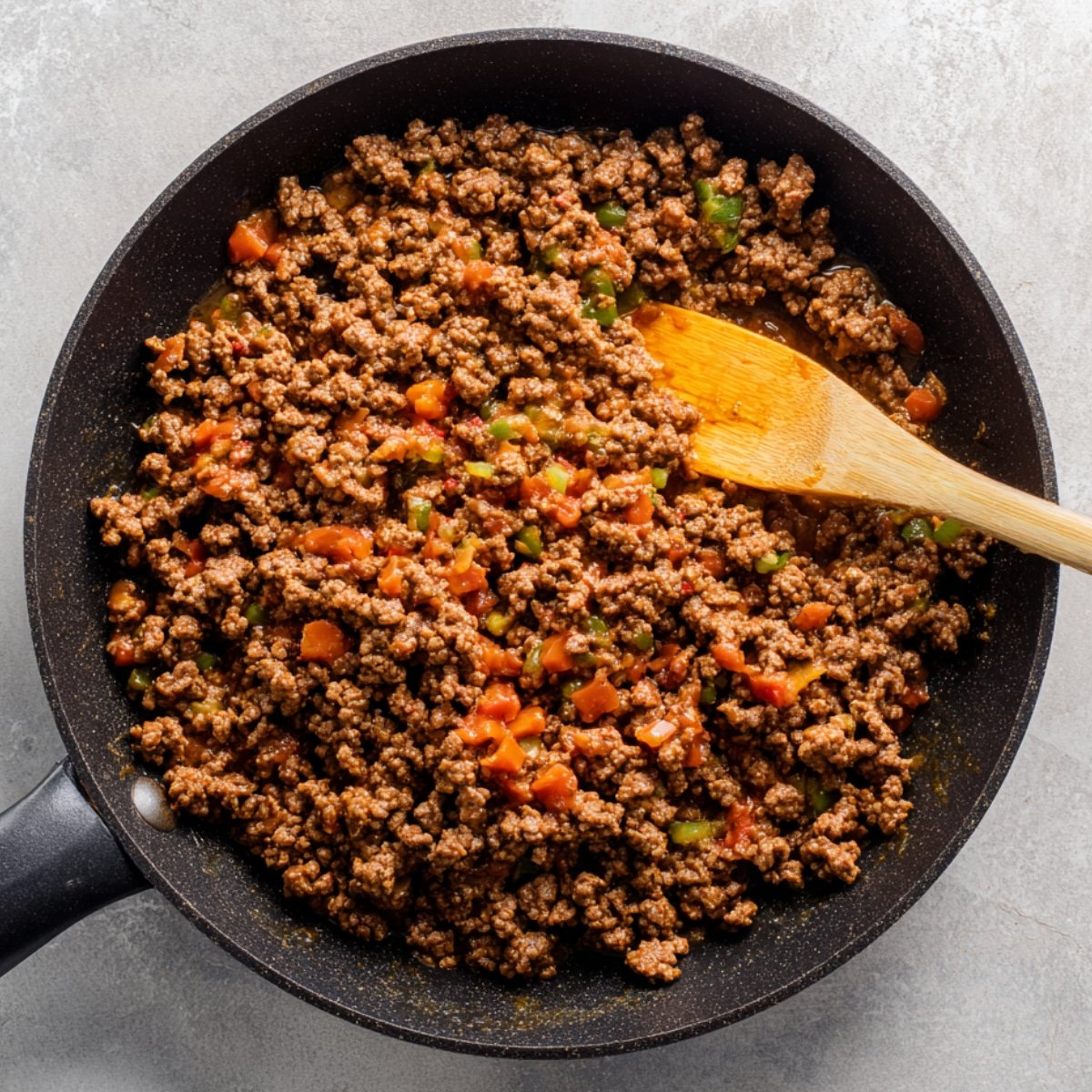 A skillet with cooked ground beef and chopped tomatoes, seasoned with green peppers and spices.