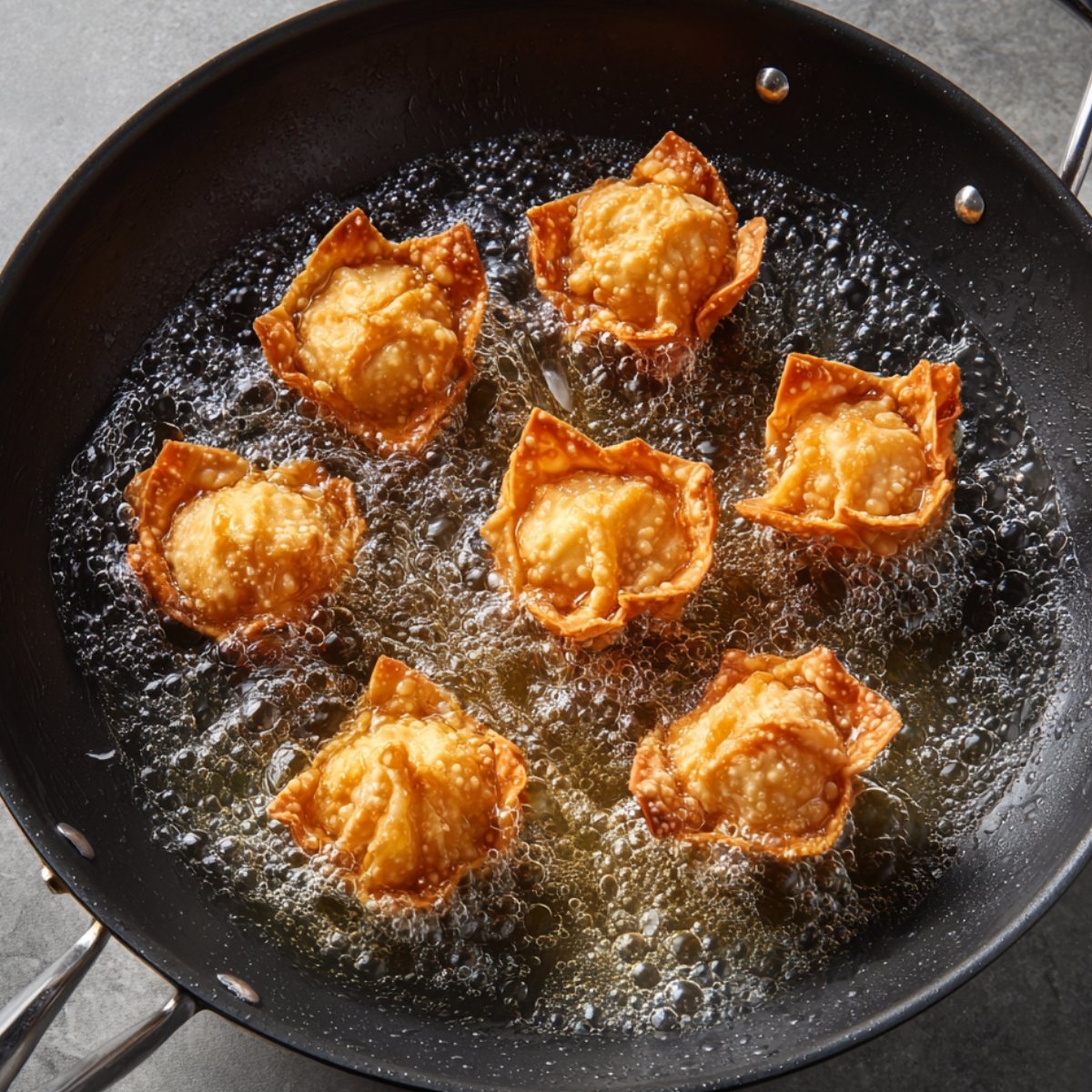 A wok filled with oil and golden, crispy wonton wrappers frying with a stuffed filling, forming crunchy Rangoon crab bombs.