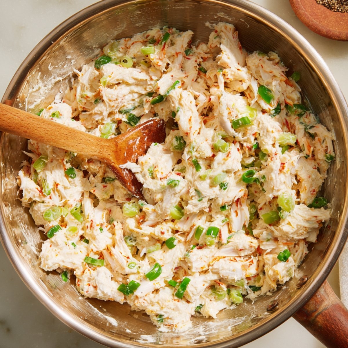 A bowl filled with a mixture of shredded crab, green onions, and other ingredients, stirred together for the filling of Rangoon crab bombs.
