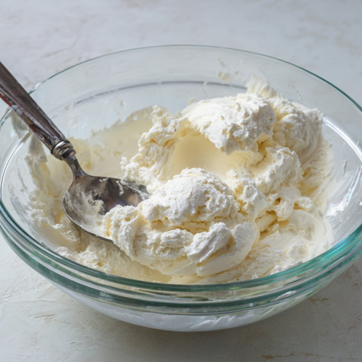 A close-up of a creamy, fluffy mixture in a glass bowl, likely whipped cream or a base for a dessert.