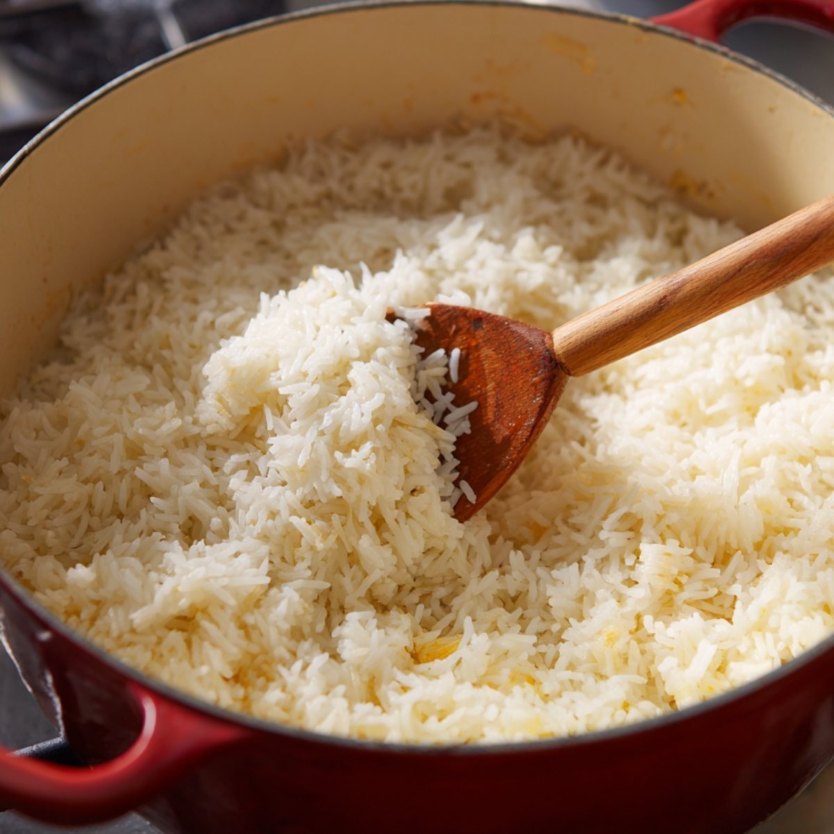 A pot of freshly cooked white rice being stirred with a wooden spoon, showing its light and fluffy texture.