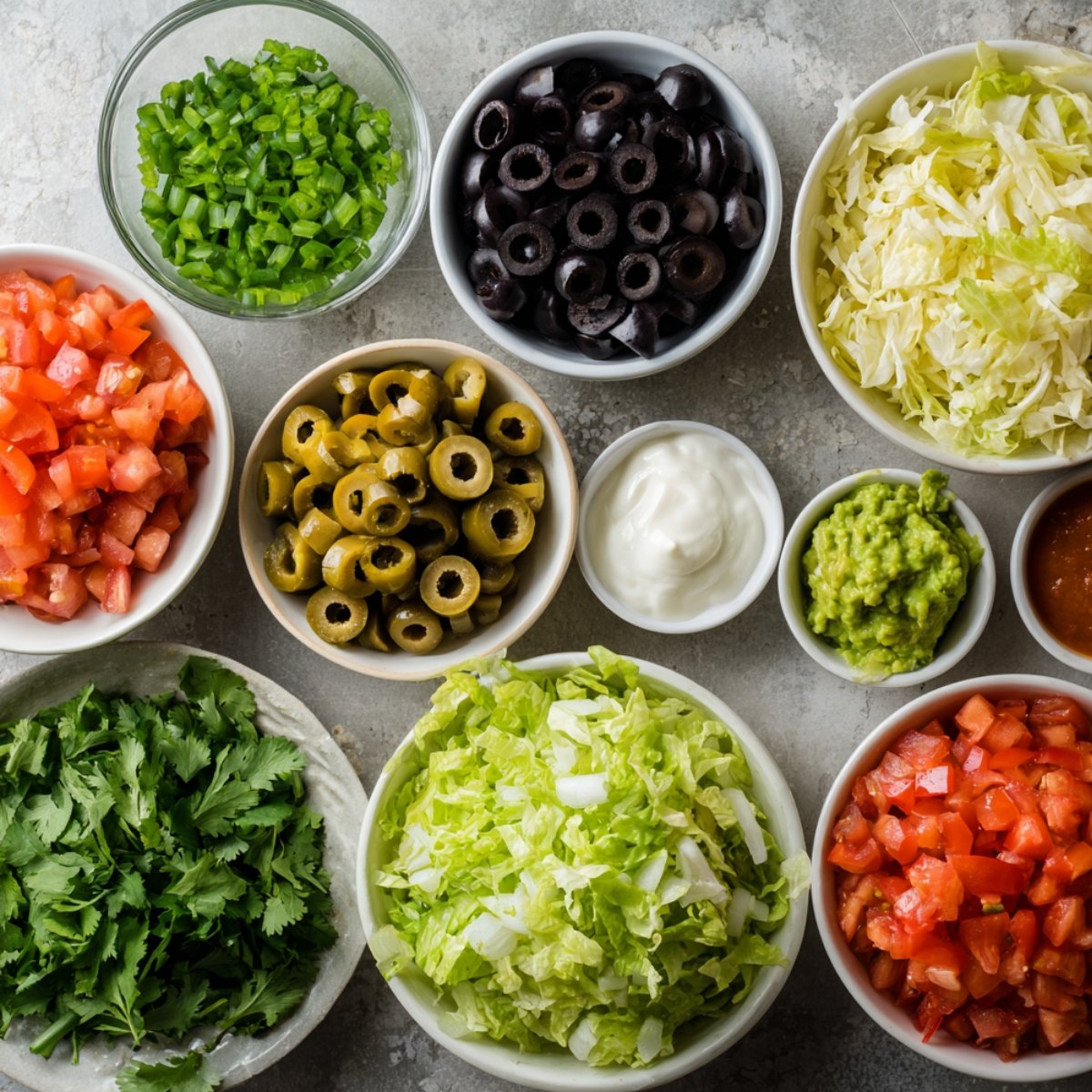 An assortment of ingredients laid out for making Mexican pizza, including flour tortillas, ground beef, shredded cheeses, salsa, taco seasoning, and more.