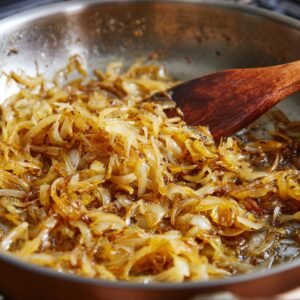 Onions caramelizing in a skillet, turning soft and golden brown with a wooden spatula stirring