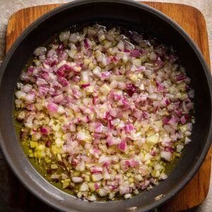 Close-up of diced onions cooking in olive oil in a pan, starting to soften and turn translucent.