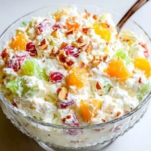 A glass bowl filled with Ambrosia Salad Recipe made of mixed fruit, whipped cream, and sprinkled nuts on top.