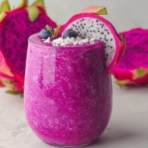 "Glass of vibrant pink dragon fruit smoothie topped with blueberries, shredded coconut, and a slice of dragon fruit."