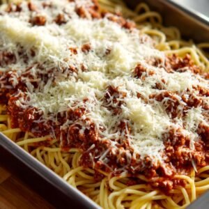 "A close-up of spaghetti topped with meat sauce and shredded mozzarella cheese in a baking dish."