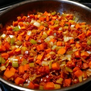 A pan with diced carrots, celery, onions, and tomato paste sautéing together.