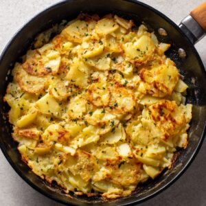 A crispy and golden-brown skillet-cooked potato dish with layers of thinly sliced potatoes, seasoned with herbs.