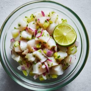 A bowl of ceviche made with fish, red onions, cilantro, and a slice of lime.