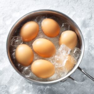 Hard-boiled eggs in their shells cooling in a bowl of ice water, helping to make peeling easier.
