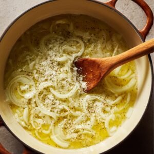 Sliced onions simmering in melted butter inside a Dutch oven, lightly seasoned with salt and pepper.