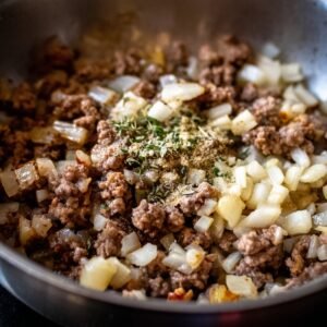 Ground beef cooking in a skillet with onions and herbs, forming the seasoned filling for cheeseburger bombs.