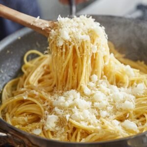 Spaghetti pasta being lifted with a wooden spoon, coated in a creamy cheese sauce and sprinkled with freshly grated cheese.