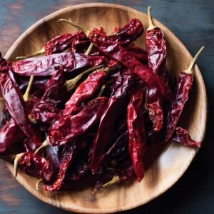"Wooden bowl filled with dried red chili peppers, typically used to make birria marinade. The chilies are glossy, wrinkled, and deep red in color."