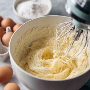 Butter and sugar creamed together in a stand mixer bowl with eggs and flour ready on the side.