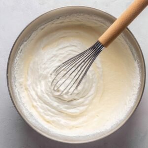 Whipped vanilla cake batter in a mixing bowl with a whisk, smooth and creamy texture.