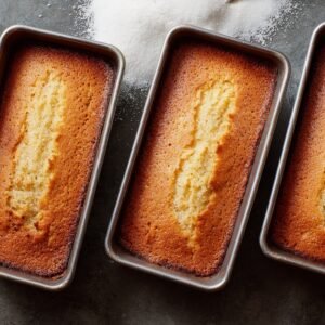 : Freshly baked golden vanilla cakes cooling in loaf pans, with sugar sprinkled on the surface.