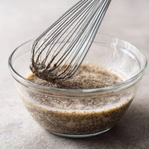 Chia seeds being whisked in a glass bowl with liquid, showing the initial stage of chia pudding preparation with seeds beginning to swell.